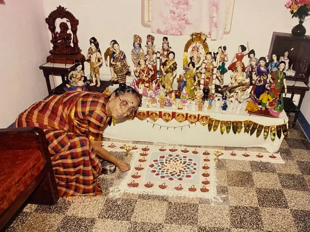 Lakshmi Santhanam kneeling to draw a rangoli in front of her Navaratri golu of dolls, 1997