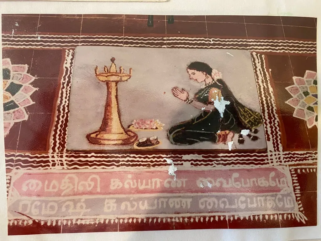 Colour photograph of a rangoli showing a lamp and a seated figure, with Tamil lettering celebrating Mythili's wedding