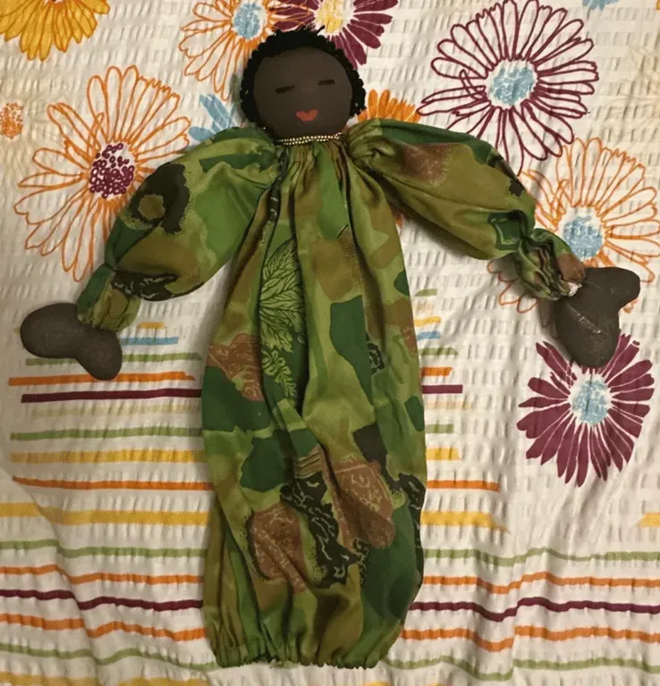 A soft cloth doll in a green patterned frock lying on an embroidered cloth