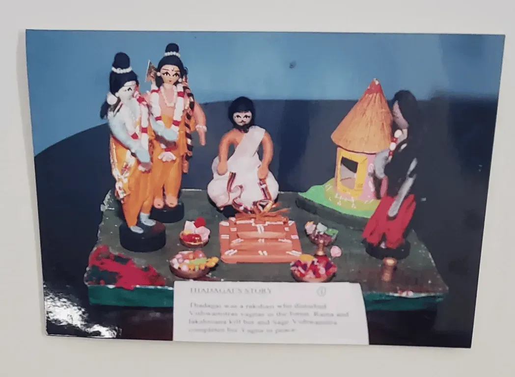 Doll scene of sages beside a thatched hut with a typed caption card, from the Ramayana series