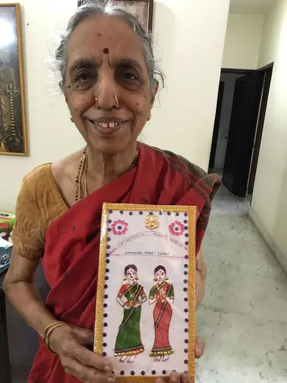 Lakshmi Santhanam in a red sari holding up a fabric-painted greeting card of two women, 2017