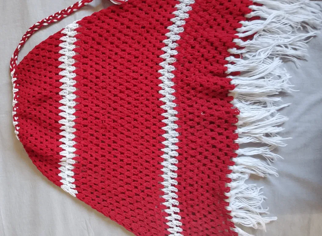 A red crochet piece with white stripes and a fringed edge