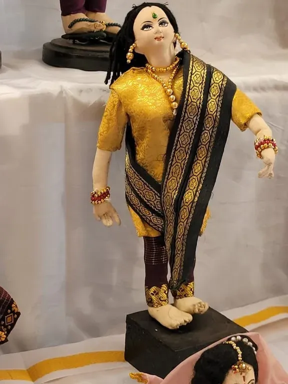 A standing cloth doll of a woman in a yellow salwar kameez with a black and gold dupatta