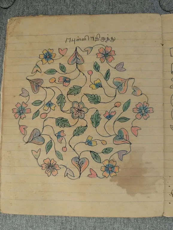 Coloured kolam of hearts and flowers arranged in a circle, on a ruled page