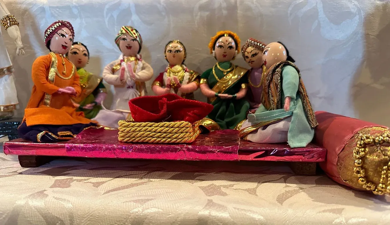 A wedding scene of cloth dolls: bride and groom seated on a dais with family members gathered round