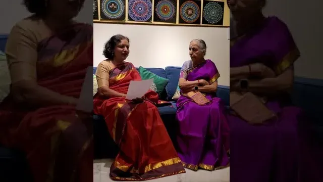 Mala in a red silk sari holding notes, sitting beside Lakshmi Santhanam in a purple silk sari on a blue sofa