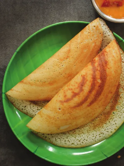 A folded dosa on a green plate with coconut chutney and sambar