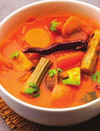 A bowl of sambar with drumstick and vegetable pieces in tamarind broth