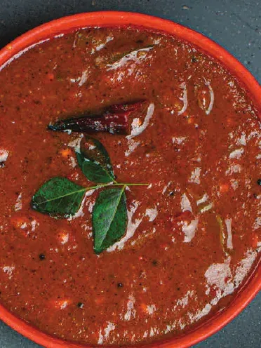 A bowl of vathal kuzhambu, a thick tamarind gravy, garnished with curry leaves