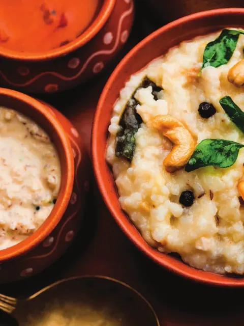 Ven Pongal in a clay bowl, garnished with cashews, curry leaves and whole peppercorns